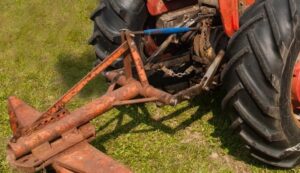 Närbild av en äldre traktors trepunktslyft med rostigt redskap