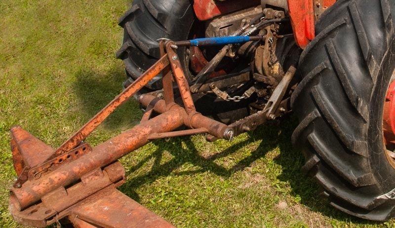 Närbild av en äldre traktors trepunktslyft med rostigt redskap