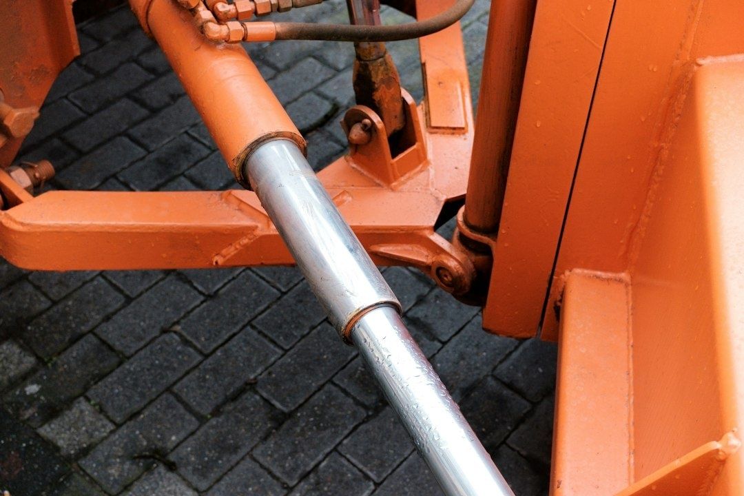 Närbild av orange hydraulcylinder och leder på en trepunktslyft